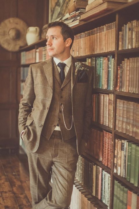 a vintage brown three piece suit with a windowpane print, a navy tie, a neutral shirt and a watch chain