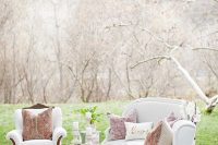 a welcoming outdoor wedding lounge with neutral seating furniture, printed pillows and a rug, a round coffee table with candles