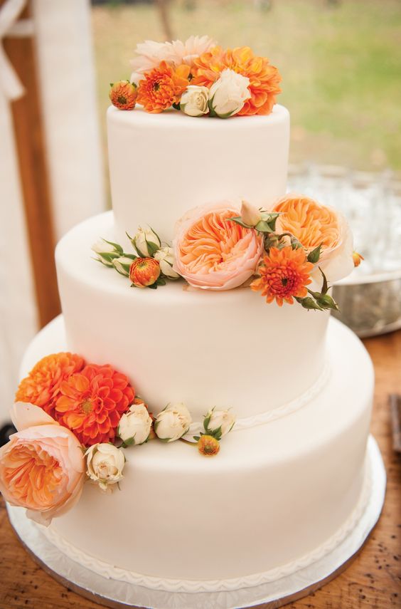 a white buttercream wedding cake decorated with blush, white and orange blooms looks chic and bold