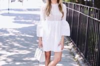 a white mini dress with a lace bodice, a plain skirt, bell sleeves of lace and plain fabric, white sneakers and a bag