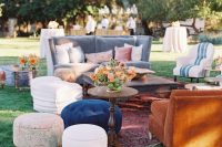 an eclectic boho wedding lounge with a grey sofa and a rust-colored seat, a couple of coffee tables, some poufs and bright blooms