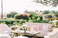 an elegant neutral wedding lounge with a tufted sofa and chairs, round poufs and a vintage coffee table, neutral blooms
