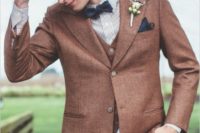 an elegant vintage groom’s look with a rust blazer and waistcoat, burgundy pants, a striped button down, a navy bow tie and a brown hat