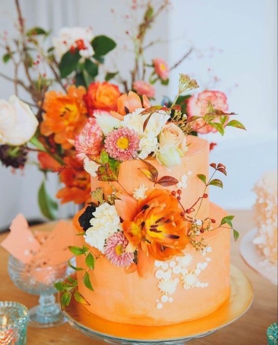 an orange wedding cake decorated with white meringues, with neutral, pink and orange blooms, berries and greenery