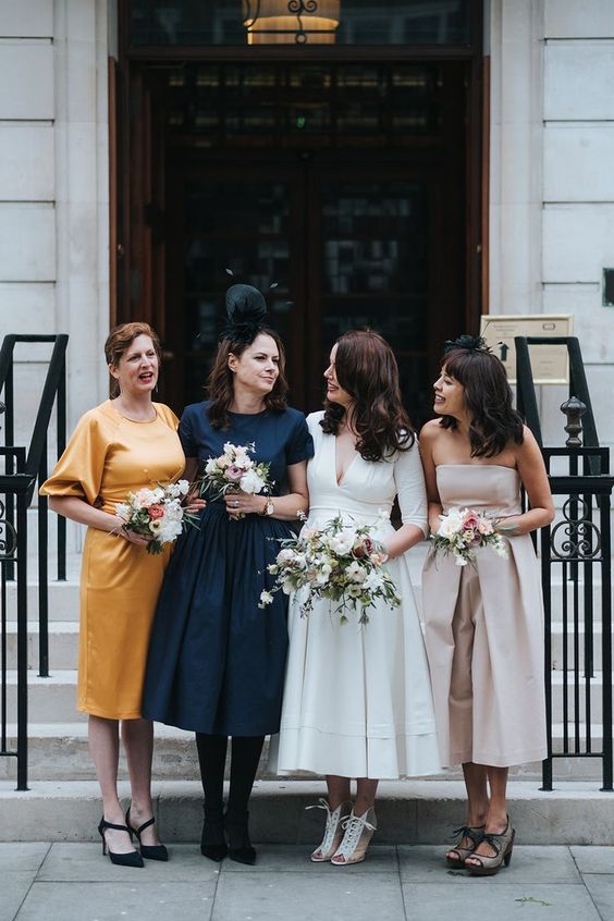 various vintage-inspired midi bridesmaid dresses in neutrals, yellow and navy, with mismatching shoes