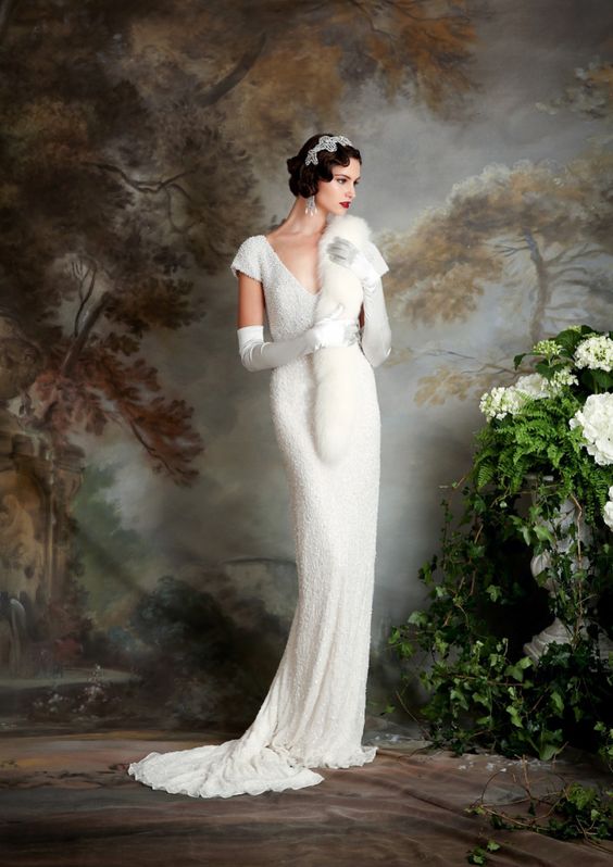 a 1920s embellished wedding dress with a V-neckline, short sleeves, a train, a faux fur scarf and an embellished headpiece plus statement earrings