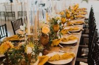 a beautiful and bright fall wedding tablescape with greenery, mustard-colored blooms and napkins, tall candles, brown glassses and greenery