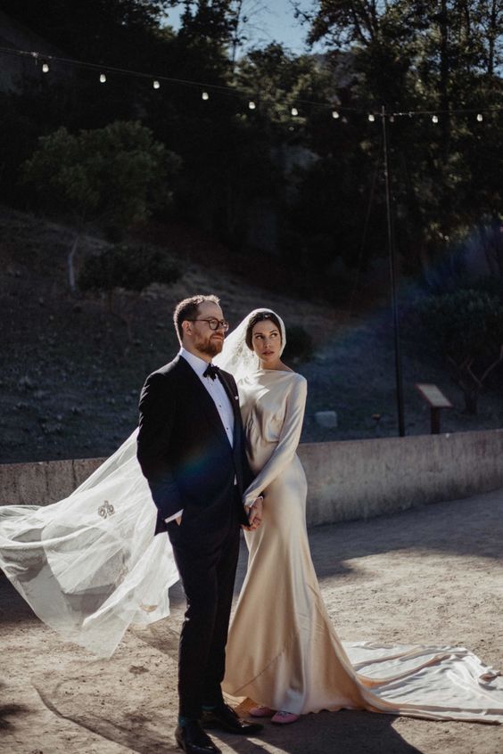 a beautiful and refined champagne-colored art deco A-line wedding dress with a high neckline and long sleeves, a long train and a veil for an art deco wedding