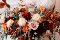 a beautiful burgundy, rust, orange, blush flower wedding bouquet with greenery for a fall bride