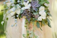 a beautiful cascading wedding bouquet with white blooms, a dark succulent, berries, blue blooms and some cascading greenery