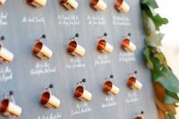 a beautiful fall seating chart of mini copper mugs on pins decorated with lush greenery and magnolia leaves