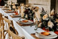 a beautiful fall wedding table setting with woven placemats, neutral linens, pastel blooms, greenery and pampas grass plus candles