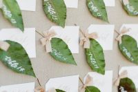a beautiful wedding seating chart of fabric and simple green leaves attached with tags and little bows