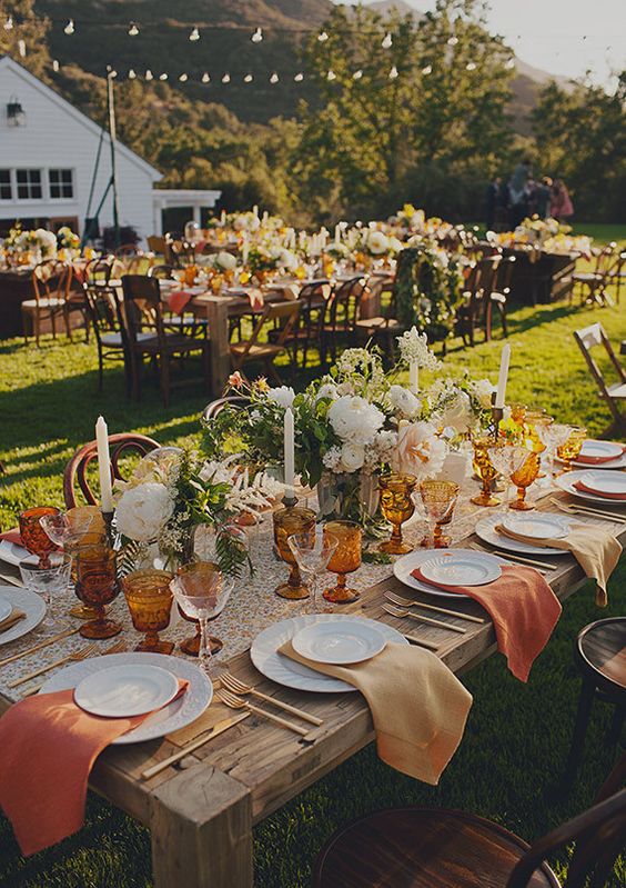 a beautiful wedding tablescape with rust and amber napkins, a floral runner, neutral blooms and greenery and amber glasses