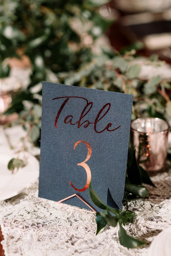 a black and copper table number paired with a lush greenery centerpiece for a modern fall tablescape