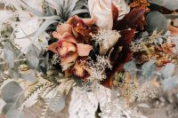 a boho fall wedding bouquet of rust, blush blooms, dark foliage and greeneyr, air plants, grasses and macrame with fringe is amazing
