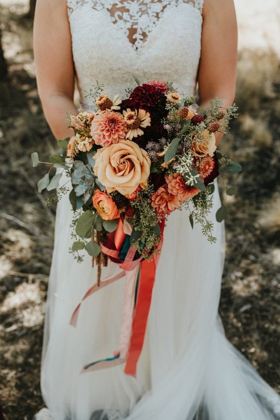 a bold and catchy wedding bouquet of rust, yellow, deep purple blooms, berries and seeded eucalyptus plus bright ribbons