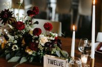 a bold and chic fall wedding centerpiece with burgundy, purple and white blooms and greenery and white candles