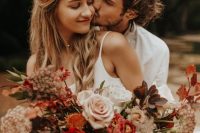 a bold and lush fall wedding bouquet of blus, rust, deep red blooms, greenery and dark foliage, grasses is a lovely idea for a boho fall wedding