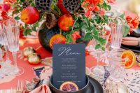 a bold fall wedding centerpiece of greenery, red blooms and fruits, some lotus blooms is lovely
