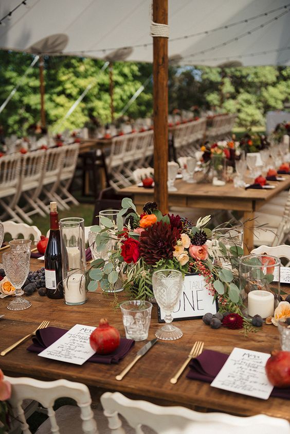 a bold fall wedding tablescape with a lush floral centerpiece, candles, pomegranates and burgundy napkins
