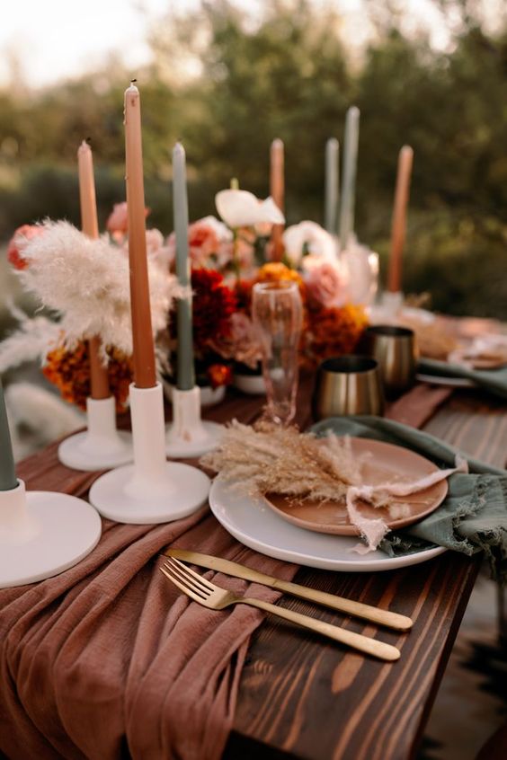 a bold fall wedding tablescape with a rust runner and grey napkins, matching candles, bold floral arrangements and gold cutlery is wow