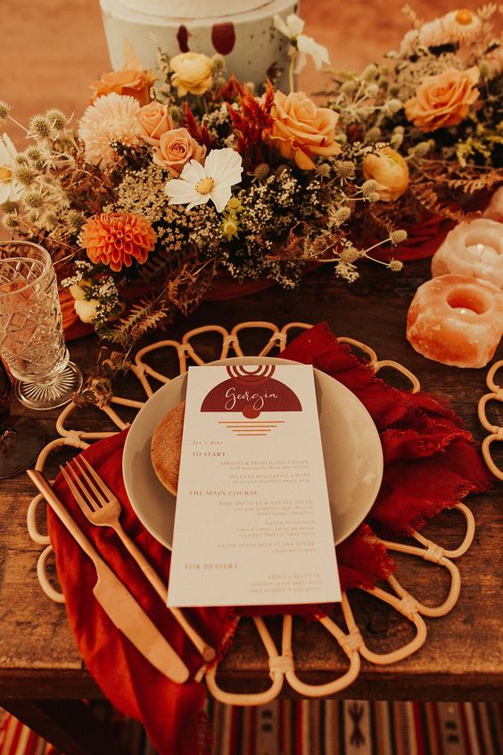 a bold fall wedding tablescape with rust, red, burgundy blooms, amber stone candleholers, a red napkin, amber cutlery and a placemat