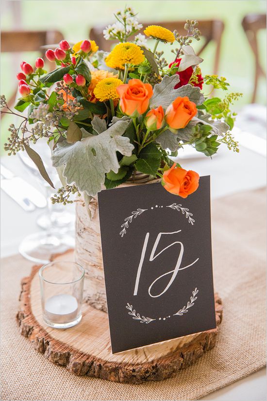 a bold rustic centerpiece of a wood slice, a candle, a chalkboard table number and a bright floral arrangement