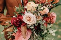 a bright fall wedding bouquet of blush, neutral, deep red and pink blooms, greenery, berries and twigs with long ribbons is amazing