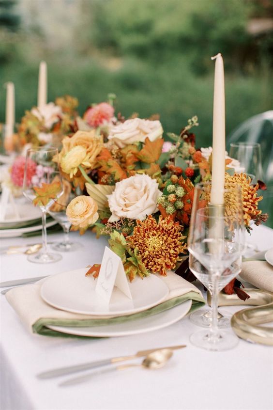 a bright fall wedding tablescape with a bold floral centerpiece with berries, white linens, candles and cool gold cutlery is wow