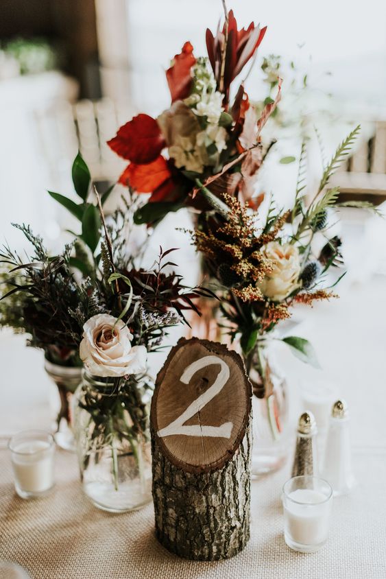 a bright rustic centerpiece of greenery and blooms, a tree branch cut with a table number for a fall tablescape