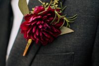 a bright wedding boutonniere of a burgundy dahlia, some greenery is a stylish idea for a fall or winter wedding