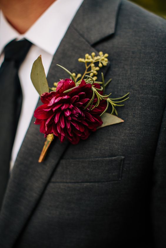 a bright wedding boutonniere of a burgundy dahlia, some greenery is a stylish idea for a fall or winter wedding