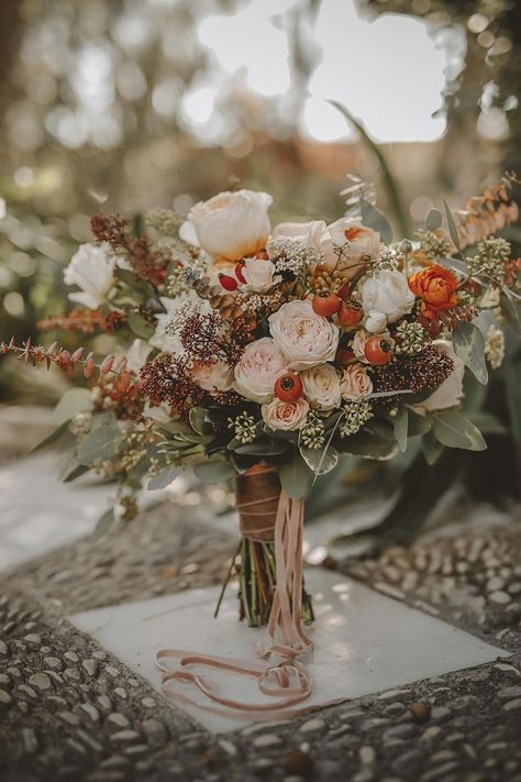 a catchy fall wedding bouquet of blush and orange flowers, berries, greenery and dark foliage plus pink ribbons is a stunning idea