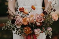 a catchy fall wedding bouquet of pale pink, rust, orange, deep purple blooms, greenery, twigs, berries is a bold and cool idea for a delicate bridal look