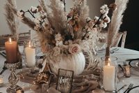 a chic neutral fall wedding tablescape with a pumpkin vase with cotton and pampas grass, candles, a taupe runner with LED lights, neutral linens