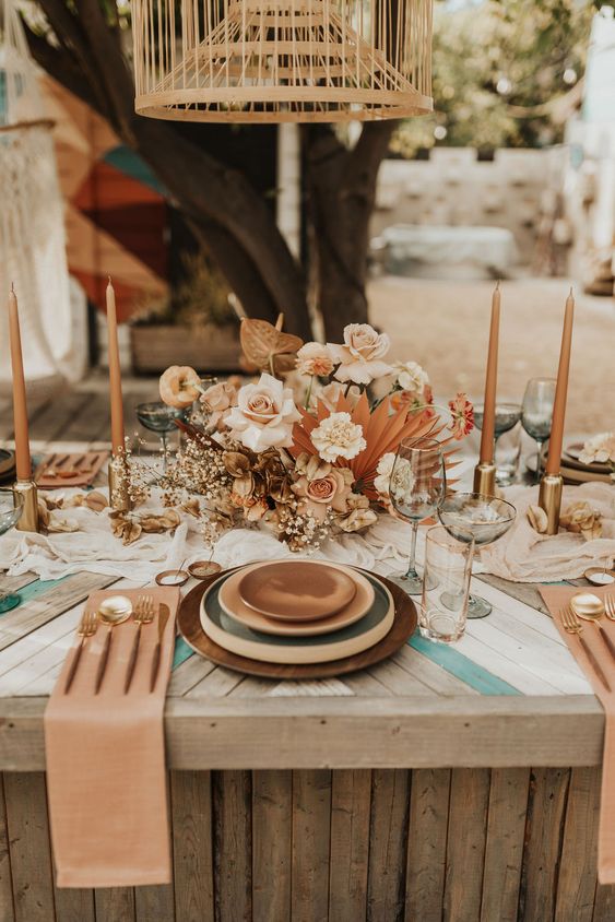a chic wedding tablescape with layered plates, a lush blush and rust floral centerpiece, rust candles and rust napkins