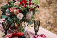 a colorful fall wedding centerpiece of greenery, blush, pink and red blooms and berries and fruits on the table