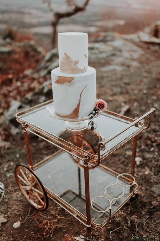 a copper cart and a white and copper marbled wedding cake with a pink rose is a stylish piece