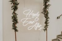 a copper wedding arch with greenery and a neon light is a lovely decoration for a modern wedding
