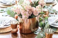 a cozy tablescape with copper hammered cups, a vase and peachy pink blooms plus wicker chargers