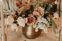 a delicate fall wedding centerpiece of a brass vase with neutral and rust-colored blooms and foliage