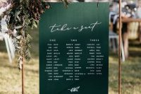 a fall wedding seating chart of a copper frame, a green chart hanging and lush greenery and acorns is lovely