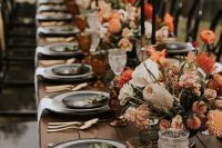 a fantastic modern wedding table setting with rust and orange florals, rust glasses, black plates and candles looks fashion-forward