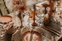 a gorgeous boho wedding tablescape with macrame placemats, rust plates, candles and florals, pampas grass and amber glasses