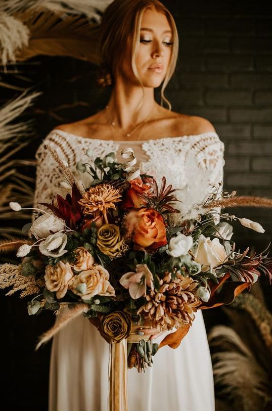 a gorgeous fall wedding bouquet of rust, light yellow, white and burgundy blooms, greenery, buny tails and dried grasses is a lovely solution for a boho bride