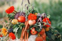 a harvest wedding centerpiece of a white bowl, bright red and orange blooms, lavender, greenery, apples, carrots and beets