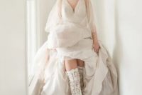 a jaw-dropping bridal look with an A-line wedding dress with a draped bodice, semi sheer puff sleeves and over the knee lace boots