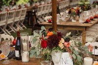 a lush fall wedding centerpiece of burgundy, red and blush blooms, grapes, plums and eucalyptus and candles