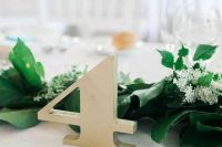a lush greenery garland with wildflowers and a simple metal table number for modern fall wedding decor